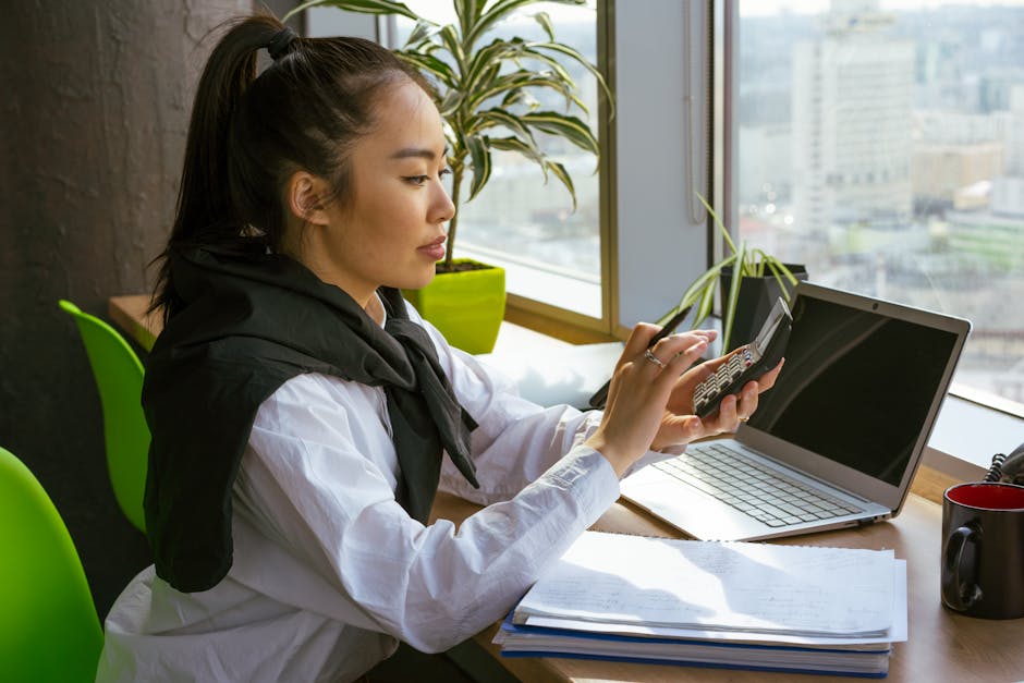 A young woman calculates finances in a modern office setting with natural light.